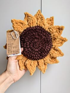 a hand holding a crocheted sunflower with a tag attached to it's center