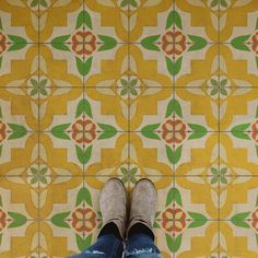 someone's feet in jeans and slippers standing on a tiled floor with yellow and green tiles