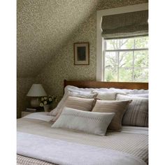 a bed sitting under a window next to a lamp on top of a wooden headboard