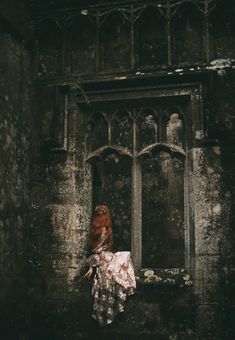 a woman with red hair is standing in an old building looking out the window at something