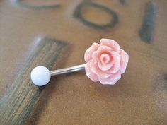 a close up of a pink flower on a metal barbell ring with a white ball