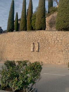 a stone wall with trees and bushes in the foreground