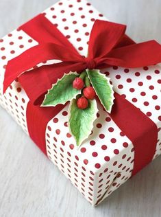 a christmas present wrapped in white and red paper with holly leaves on top, sitting on a table