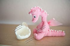 a crocheted pink dragon sitting next to a small white bowl on a table