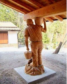 a statue of a man holding a bucket under a wooden structure with trees in the background