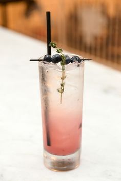 a drink with blueberries and an olive sprig on the rim is sitting on a table