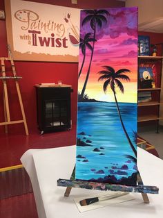 an easel painted with palm trees and the ocean in front of a sign that says painting with twist