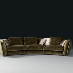 a curved couch with pillows on it in front of a black wall and grey floor