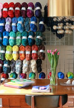 there are many skeins of yarn hanging on the wall next to a vase with tulips