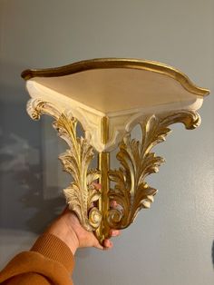 a person holding up a light fixture with gold leaf designs on it's side