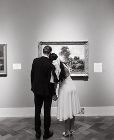 a man and woman standing in front of an art piece looking at the painting on display