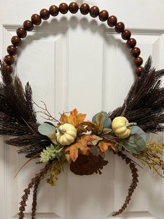 a wreath with leaves, flowers and pumpkins hanging on the front door for fall