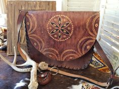 Whether you're a cowgirl or a western boho chic Fashionista, this tooled leather purse is an accessory you need. It is versatile enough to go in your spring wardrobe or even fall. The exterior is warm brown with the tooling done on the flap of the purse. The interior is very basic with no pockets or pouches. the strap on this tool leather purse is adjustable with a buckle for varying lengths. this purse measures approximately 11 in wide at its widest point. it stands 9.5 in in height and is approximately 2.5 in depth. it is important to notice the stitching is not done with leather stitching. This simple hand stamped leather bag would accent beautifully a western outfit that likes you would see on Yellowstone. It would also be a wonderful accessory for any cowgirl for western boho chic Fas Western Style Hand Tooled Brown Shoulder Bag, Western Style Brown Hand Tooled Shoulder Bag, Western Style Hand Tooled Brown Bag, Western Style Brown Bag With Concho, Western Hand Tooled Travel Bag, Western Style Hand Tooled Shoulder Bag For Travel, Western Brown Shoulder Bag With Adjustable Strap, Western Style Hand-tooled Travel Bag, Western Brown Satchel Shoulder Bag