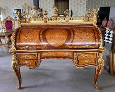 an ornate wooden desk with gold trimmings and carvings on the top, surrounded by other antique furniture