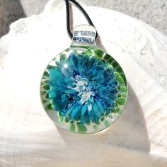 a blue and green flower is in a glass ball on a black cord necklace, sitting on a white rock