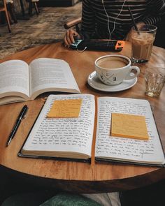 two open notebooks sitting on top of a wooden table next to a cup of coffee