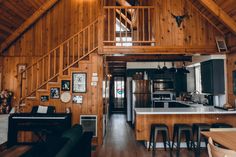 a kitchen and living room in a cabin with wood paneling on the walls, wooden stairs leading up to an upper floor