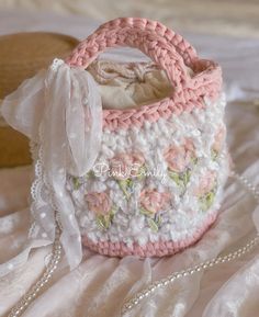 a pink and white crocheted purse sitting on top of a bed