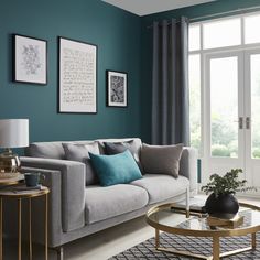 a living room with teal walls and grey couches in front of a window