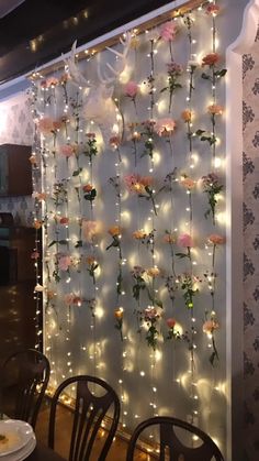 the flowers are hanging on the wall behind the chairs in the dining room, with fairy lights strung all over it