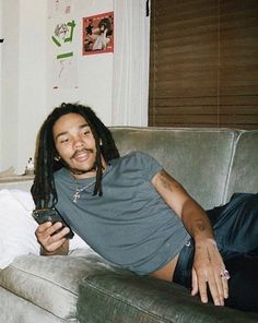 a man with dreadlocks sitting on a couch holding a cell phone in his hand