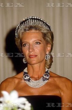 an older woman wearing a tiara and pearls in front of a table with flowers