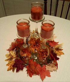 two glasses filled with liquid sitting on top of a table covered in leaves and candles