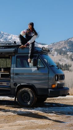 a woman sitting on the roof of a van with her skis strapped to it