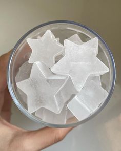 a hand holding a glass bowl filled with ice cubes and star shaped snowflakes