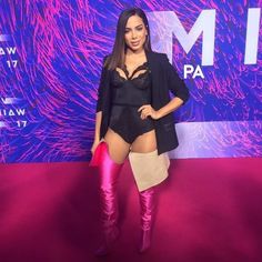 a woman standing in front of a purple background wearing thigh high boots and a black blazer