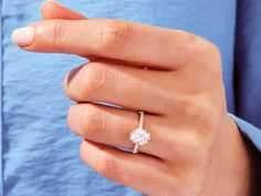 a woman's hand with a diamond ring on her left hand and a blue shirt behind her