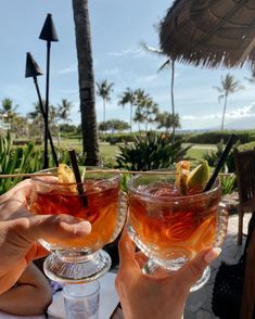 two people holding up wine glasses with drinks in them on a table near the beach