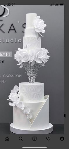 a three tiered white wedding cake with flowers on the top and bottom, in front of a gray background