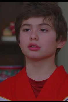 a young boy in a red shirt looking at the camera with an intense look on his face