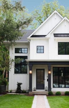 a white house with black trim on the front door and windows, grass in front