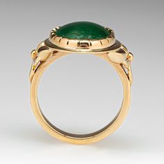 This wonderful ring is centered with one (1) oval cabochon cut natural jadeite jade set into a closed back scalloped bezel setting. Engraved floral details accent the shoulders of the ring. The ring measures 20.6mm at the top, rises 5.9mm above the finger, tapering to 3.5mm wide and 1.6mm thick at the base of the shank. This ring is currently a size 7. The jade shows overall wear on the surface. Elegant Jade Ring With Round Band, Elegant Green Domed Jewelry, Elegant Round Band Jade Jewelry, Elegant Domed Emerald Ring, Formal Cabochon Chrysoprase Jewelry, Elegant Green Intaglio Ring, Formal Oval Jade Emerald Ring, Elegant Jade Cabochon Rings, Elegant Jade Rings With Cabochon