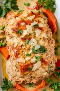 Baked chicken breast topped with cheese and herbs, served with cooked carrots and peas in a creamy sauce.