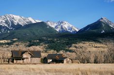 an old barn sits in the middle of a field with mountains in the back ground