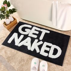 a bathroom rug with the words get naked on it next to slippers and potted plant