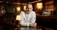 a man sitting at a table in front of a bar with lights on the wall