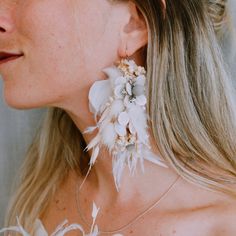 a woman with long blonde hair wearing large white feathers and flowers on her earring