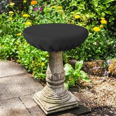 a stone pedestal with a black cover on it in front of some flowers and bushes