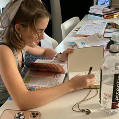 a woman sitting at a table writing on a piece of paper next to a bottle of water