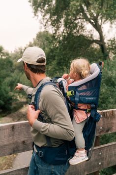 a man carrying a child in a baby carrier while standing next to a wooden fence