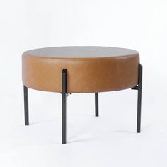 a small round table with black legs and a tan leather seat on the bottom, against a white background