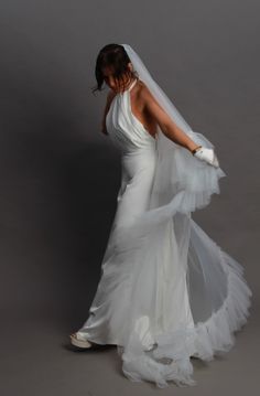 a woman in a white wedding dress is holding her veil over her head and looking down