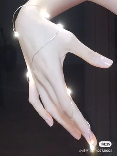 a woman's hand with white nails and lights attached to it, in front of a black background