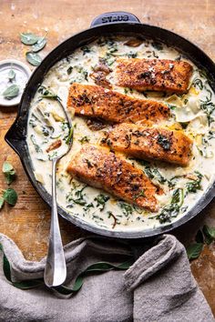 three salmon fillets in a skillet with cream sauce and spinach on the side