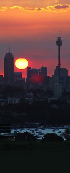 the sun is setting over a city with tall buildings in the foreground and water below