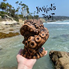 a person holding up a carved animal head in front of the ocean